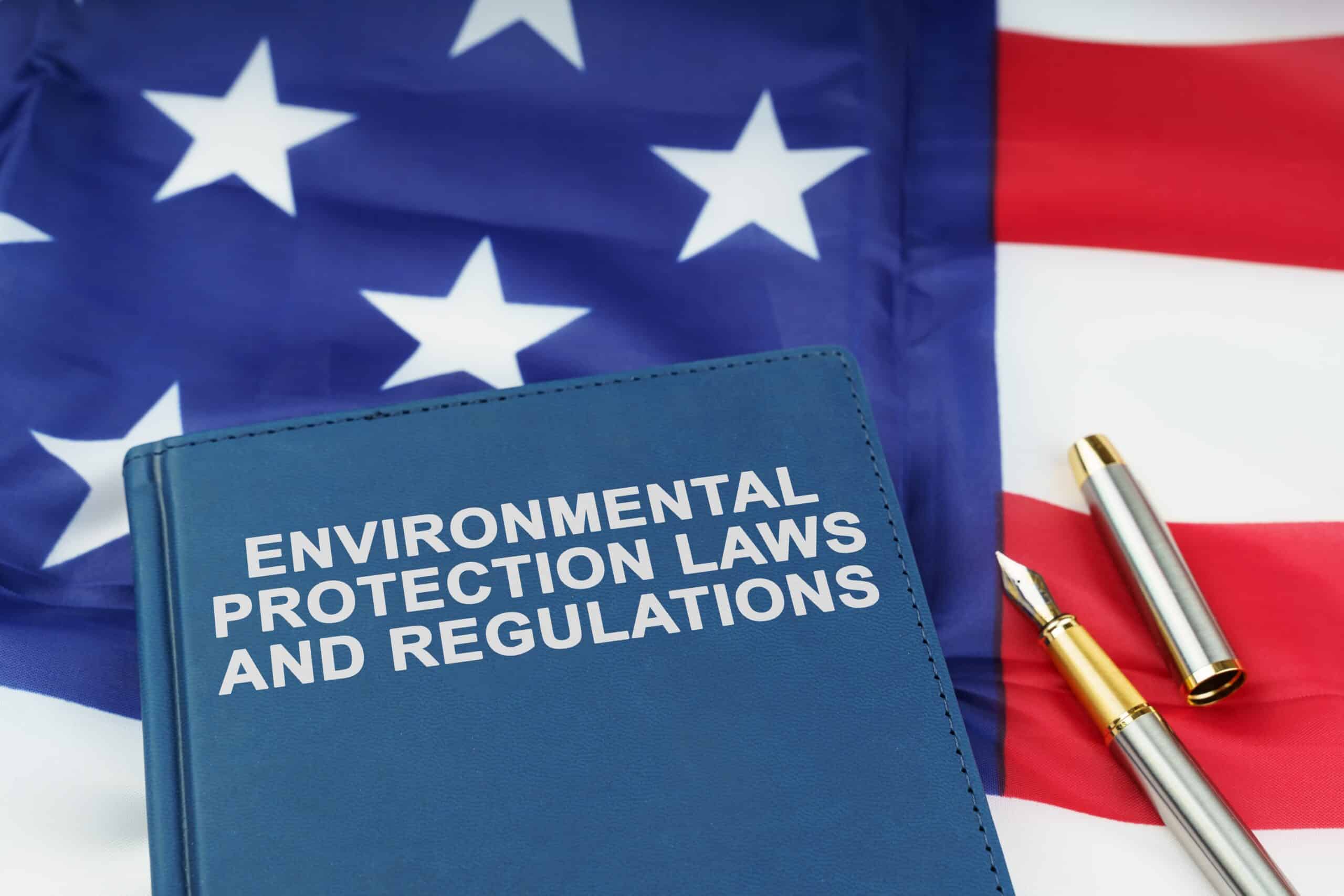 Book titled “Environmental Protection Laws and Regulations” on top of an American flag with a fountain pen, symbolizing U.S. EPA asbestos reporting requirements for manufacturers, importers, and distributors.